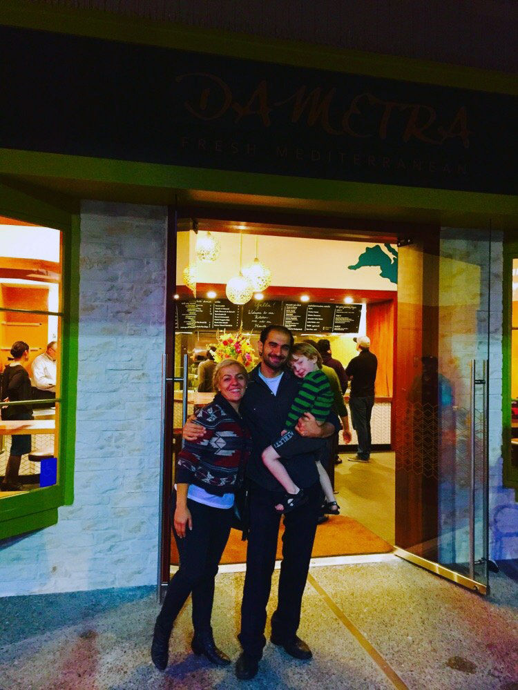 Restaurant owner posing and smiling with a patron and her son outside of the restaurant.