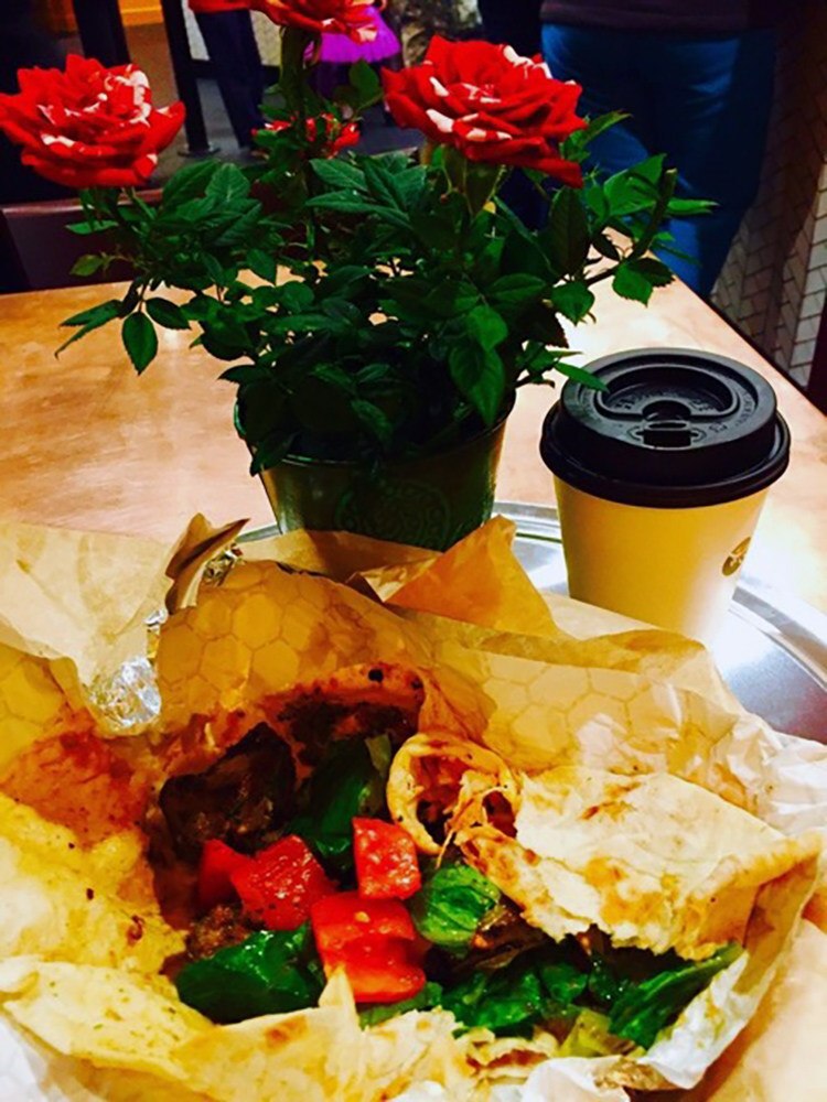 Tabletop showing an unwrapped partially savored meal, a to-go cup and red roses.