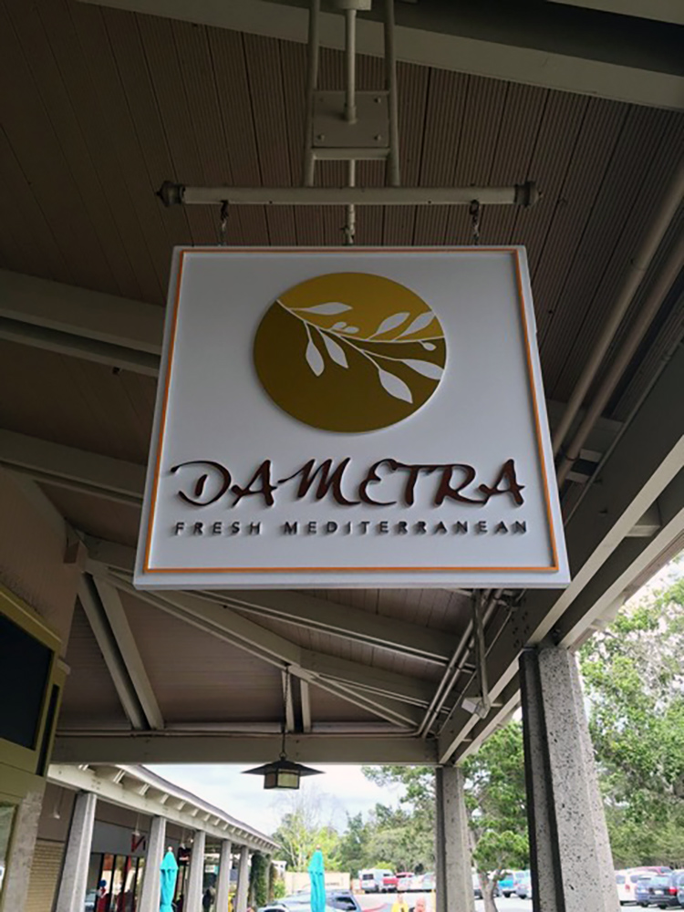 Wooden sign with logo of olive branch and Dametra Fresh Mediterranean hanging outside of restaurant.